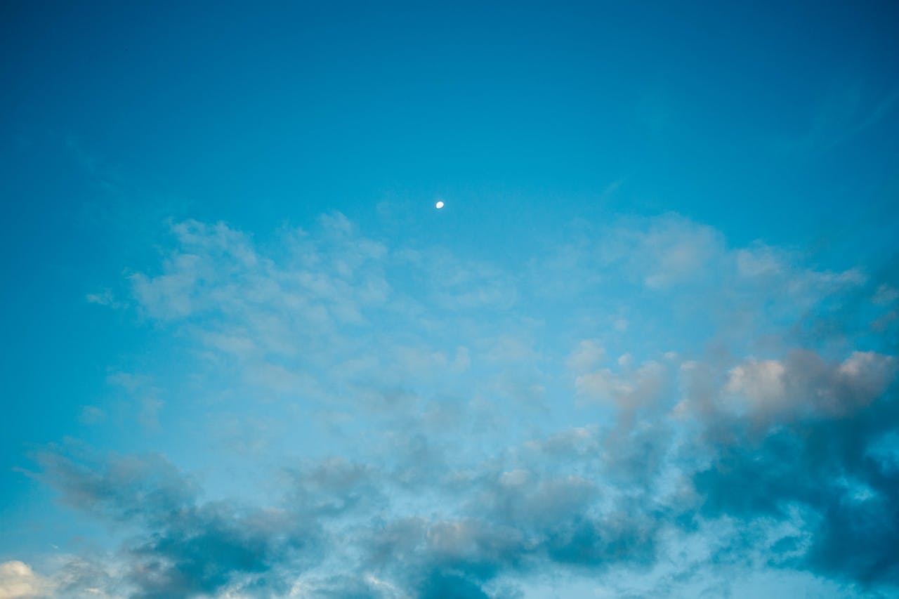 Tiny Moon in amazing vibrant blue sky covered with highlighted clouds in evening